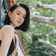 Chinese-born New Zealand author Chloe Gong, wearing a black top, poses looking over her shoulder with a tree in the background.